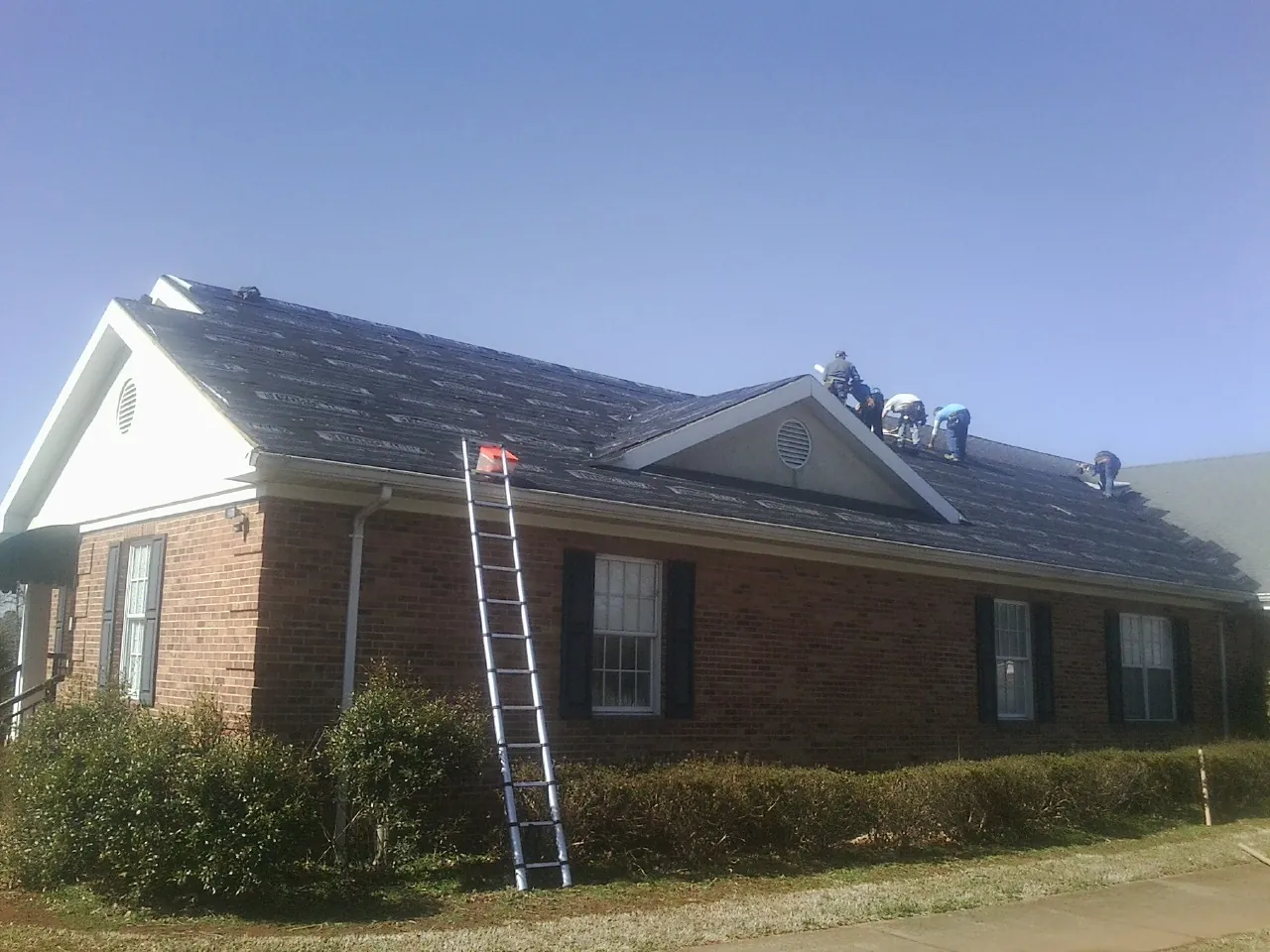 Crew tearing shingles off a brick ranch roof with a ladder set — Emergency Roof Repair work by our crew in Liberty Center
