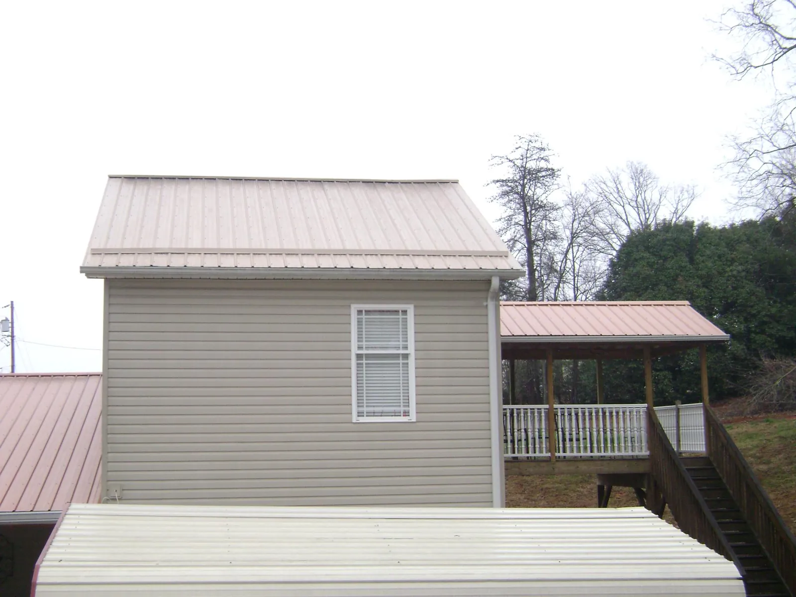 Tan metal roofs on a two story addition and attached porch, from a Roof Replacement job in Liberty Center